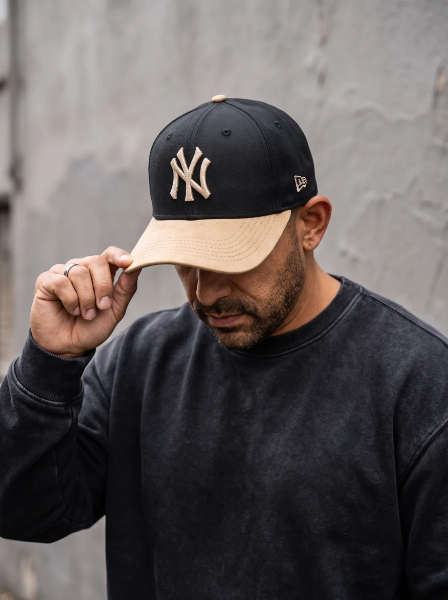 Gorra negra con monograma claro y visera en tono arena, combinada con un look urbano.